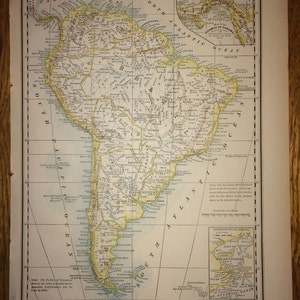 May include: A vintage map of South America, showing the countries and major cities. The map is printed in brown, yellow, and blue ink on a cream-coloured background. The map is titled "Atlas of the World" and includes a key for understanding the map's symbols.