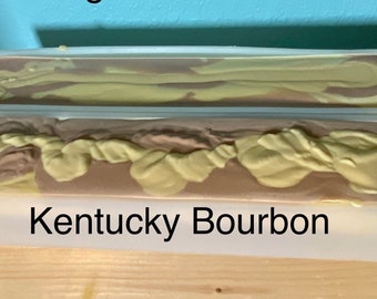 May include: Two bars of handmade soap in clear plastic molds. The soap is a swirl of brown and yellow. The bottom bar has the text "Kentucky Bourbon" printed on the mold.