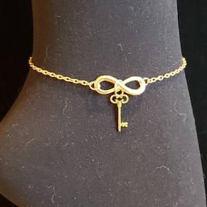 May include: Gold ankle bracelet with an infinity symbol charm and a key pendant.