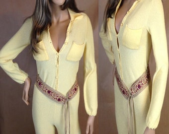 May include: A yellow jumpsuit with long sleeves and a button-up front. The jumpsuit has two pockets on the chest and a brown belt with a red and gold pattern.