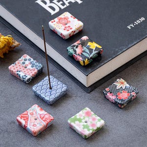 Op de afbeelding: Een set van drie keramische mokken met een gespikkelde, matte afwerking. De mokken zijn in crème, lichtgrijs en donkergrijs. Elke mok heeft een eenvoudig, minimalistisch ontwerp.