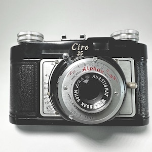 May include: A vintage black Ciro 35 camera with silver accents. The camera features a Wollensak Anastigmat lens and the text "Ciro 35" on the top. The lens has f/4.5 and 50mm markings. The camera has a classic, retro design.