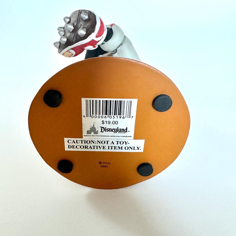 Peut inclure: Figurine d&eacute;corative avec une base marron et une figurine portant un casque rouge et blanc. La base porte une &eacute;tiquette indiquant &laquo;&nbsp;ATTENTION&nbsp;: PAS UN JOUET - ARTICLE D&Eacute;CORATIF UNIQUEMENT&nbsp;&raquo;. La figurine est de Disneyland.