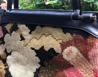 May include: A black leather tote bag with a floral tapestry design. The tapestry features white, red, and brown flowers on a black background.