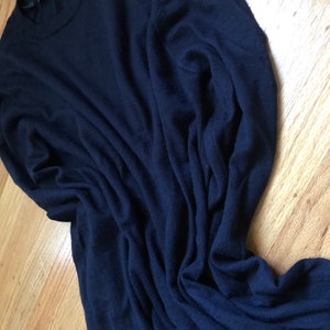 K&ouml;nnte beinhalten: Ein dunkelblauer Langarm-Pullover aus weichem, gestricktem Stoff. Der Pullover ist gefaltet und liegt flach auf einer Holzoberfl&auml;che.