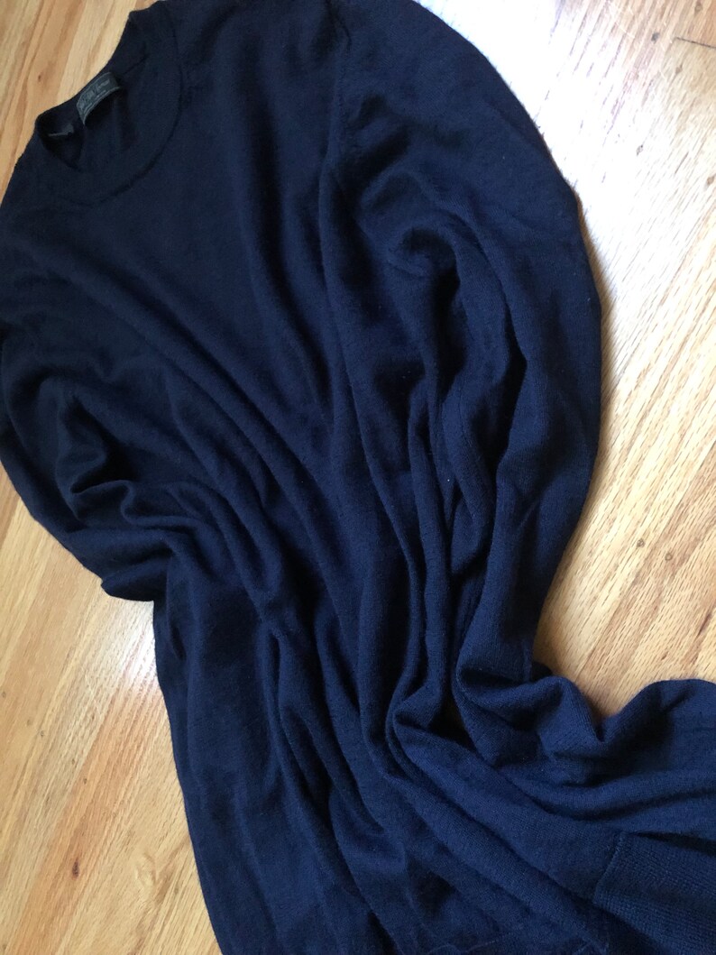 K&ouml;nnte beinhalten: Ein dunkelblauer Langarm-Pullover aus weichem, gestricktem Stoff. Der Pullover ist gefaltet und liegt flach auf einer Holzoberfl&auml;che.
