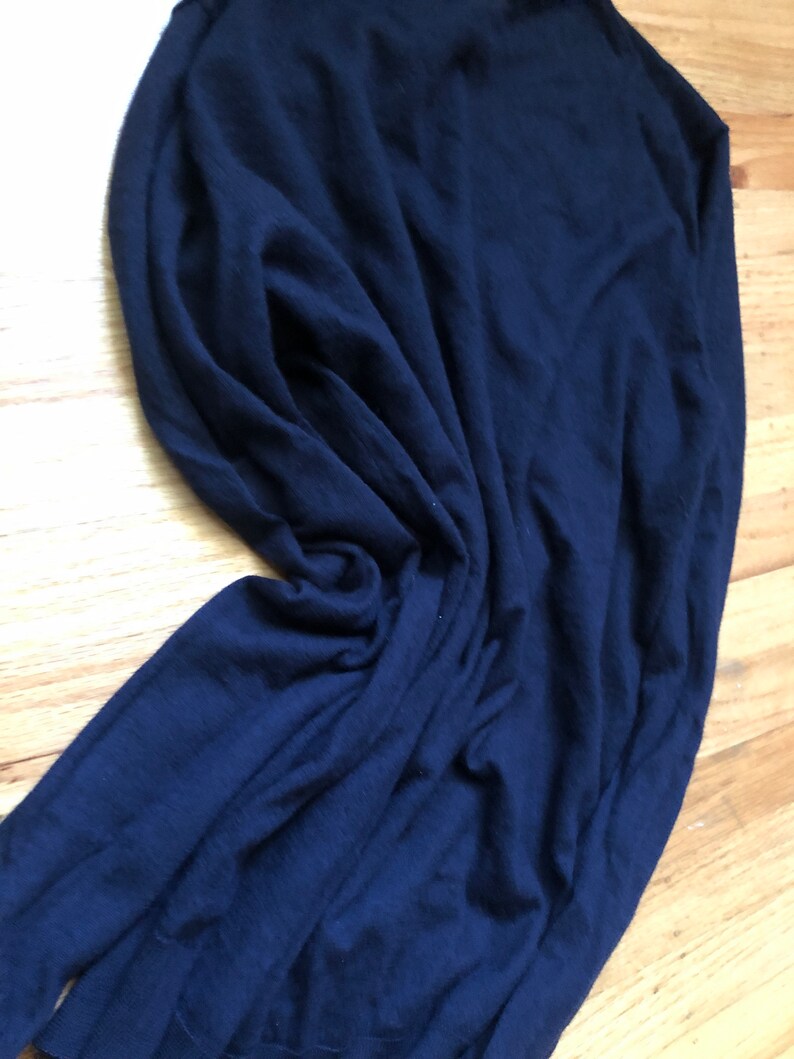 K&ouml;nnte beinhalten: Ein dunkelblauer Langarm-Pullover aus weichem, gestricktem Stoff. Der Pullover ist gefaltet und liegt flach auf einer Holzoberfl&auml;che.