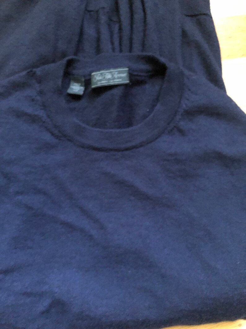 K&ouml;nnte beinhalten: Ein marineblauer Pullover mit einem kleinen, dunklen Etikett mit der Aufschrift "J.Crew" auf der Vorderseite.