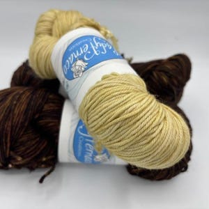 May include: Close-up of three skeins of yarn in shades of brown and yellow. One skein is a light yellow, and the other two are a dark brown with lighter brown flecks. The yarn is labeled with the text "Jemaco Creations".