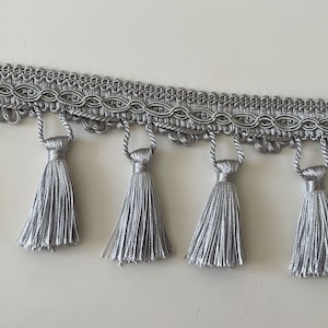 Peut inclure: Garniture argentée avec une tresse décorative et une rangée de glands.