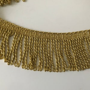 Op de afbeelding: Gouden metallic franje trim met een gedraaid koordontwerp. De franje is ongeveer 2,5 cm lang.