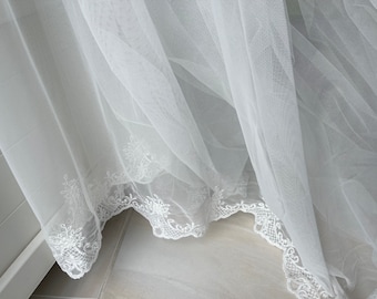 May include: White sheer curtains with a delicate lace trim. The curtains are gathered and draped, creating a soft and romantic look.