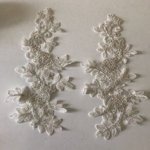 Peut inclure: Deux appliques en dentelle ivoire avec des motifs floraux et des perles. Les appliques sont parfaites pour ajouter une touche d'élégance aux robes de mariée, aux accessoires de mariée ou à d'autres projets d'artisanat.