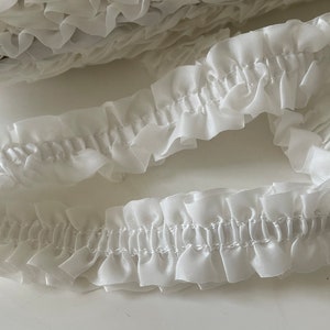 May include: White ruffled trim with a delicate, gathered texture. This trim is perfect for adding a touch of elegance to any project.