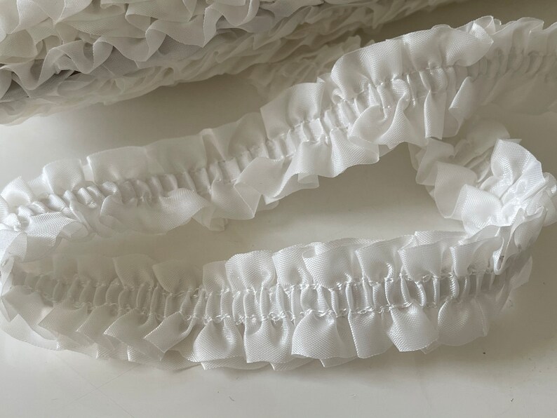 May include: White ruffled trim with a delicate, gathered texture. This trim is perfect for adding a touch of elegance to any project.