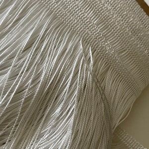 Op de afbeelding: Witte franje trim met een zachte, zijdeachtige textuur. De franje is strak geweven en heeft een uniforme lengte.