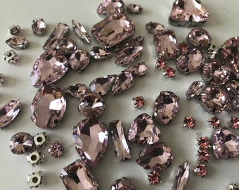 Könnte beinhalten: Eine große Auswahl an rosafarbenen Glas-Straßsteinen in verschiedenen Formen und Größen. Die Strasssteine haben eine silberne Rückseite und sind perfekt zum Basteln und für die Schmuckherstellung.