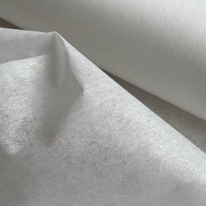 May include: White interfacing fabric, a type of fusible bonding material used in sewing and crafts. The fabric is rolled up and the edges are visible.