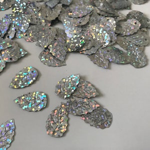 Peut inclure: Une dispersion de paillettes argentées irisées en forme de feuille avec un motif en relief.