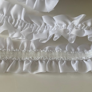 May include: White ruffled trim with an elastic backing. The trim is made of a soft, silky fabric and is perfect for adding a touch of elegance to any project.