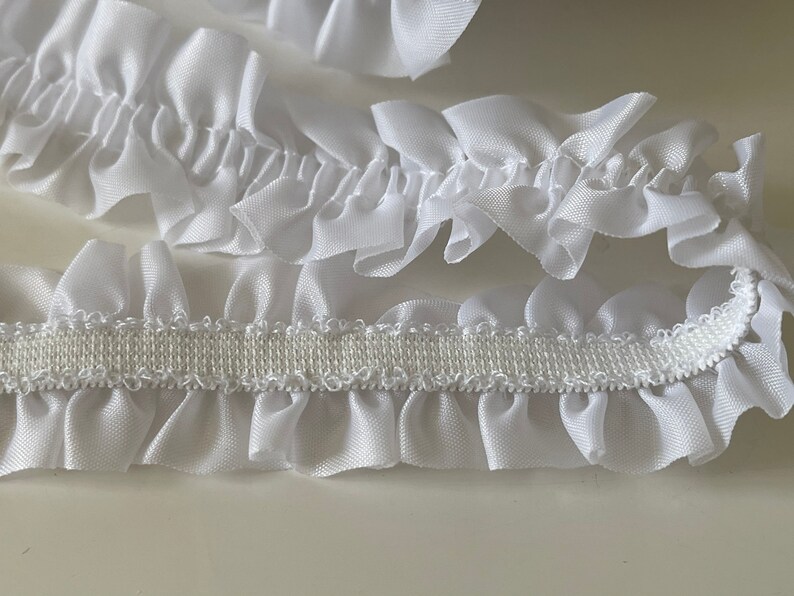 May include: White ruffled trim with an elastic backing. The trim is made of a soft, silky fabric and is perfect for adding a touch of elegance to any project.