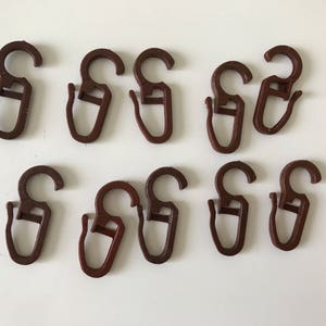 May include: Ten brown plastic curtain hooks with a simple design. The hooks are all the same size and shape.
