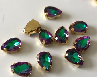 May include: A group of 10 iridescent green and purple teardrop-shaped rhinestones with gold settings.