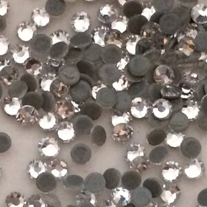 Könnte beinhalten: Nahaufnahme einer großen Menge durchsichtiger Glas-Straßsteine. Die Strasssteine sind auf einer weißen Oberfläche verstreut.