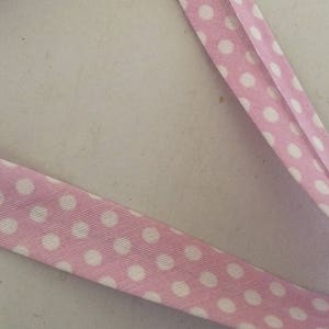 Peut inclure: Ruban rose avec des pois blancs. Le ruban est plié en deux et les pois sont espacés uniformément.