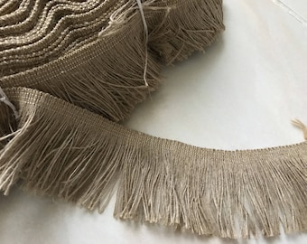 May include: A roll of tan-colored fringe trim with long, loose strands. The trim is made of a woven material and is tightly rolled. The fringe is a light brown color and is ideal for adding a decorative element to various craft projects.