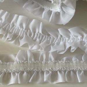 May include: White ruffled trim with an elastic backing. The trim is made of a soft, silky fabric and is perfect for adding a touch of elegance to any project.
