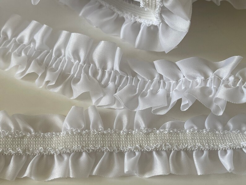 May include: White ruffled trim with an elastic backing. The trim is made of a soft, silky fabric and is perfect for adding a touch of elegance to any project.