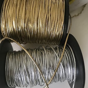 May include: Two spools of metallic cord, one gold and one silver, are wound around black plastic spools.