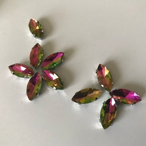 Puede incluir: Un conjunto de ocho piedras de cristal de imitación en forma de marquesa iridiscentes con engastes plateados. Las piedras de cristal de imitación tienen un efecto arcoíris con tonos de verde, rosa y morado.