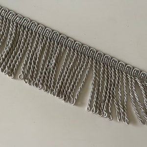 May include: Silver twisted fringe trim with a woven pattern. The fringe is approximately 2.5 cm long.