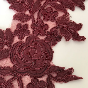 Op de afbeelding: Bordeauxkleurige kantstof met een bloemenpatroon met een grote roos en kleinere bloemen. De kant is delicaat en ingewikkeld, met een zacht, romantisch gevoel.