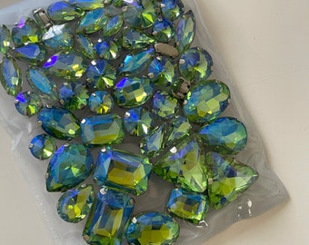 May include: A large assortment of green and blue iridescent glass rhinestones in various shapes and sizes. The rhinestones are packaged in a clear plastic bag.
