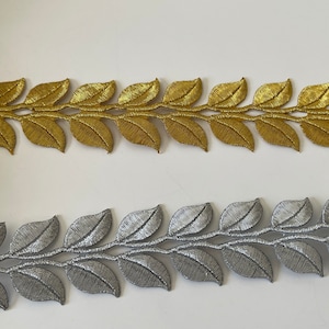 Può includere: Due passamanerie decorative a forma di foglie, una dorata e una argentata. Le foglie sono dettagliate con venature strutturate e sono attaccate a un sottile stelo. Ideali per abbellire abbigliamento, accessori o progetti di decorazione.