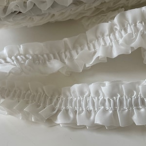 May include: White ruffled trim with a gathered look. The trim is made of a soft, delicate fabric and is perfect for adding a touch of elegance to any project.