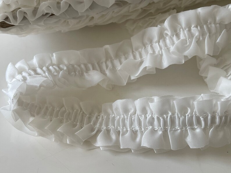 May include: White ruffled trim with a gathered look. The trim is made of a soft, delicate fabric and is perfect for adding a touch of elegance to any project.