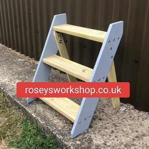 May include: A grey wooden step stool with three shelves. The stool is made of wood and has a grey paint finish. The stool is standing on a concrete surface. The text "roseysworkshop.co.uk" is visible on the stool.