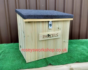 Può includere: Un contenitore per pacchi in legno con un tetto grigio strutturato e un fermo in metallo. La scatola è realizzata in legno chiaro e riporta la scritta "PARCELS" su un piccolo cartello di legno.