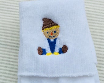 May include: White cotton socks with an embroidered scarecrow design. The scarecrow is wearing a brown hat, a blue shirt, and yellow pants.