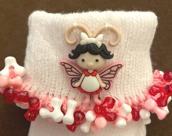 May include: White baby socks with a pink and white fairy button embellishment. The socks are trimmed with red and white beads.