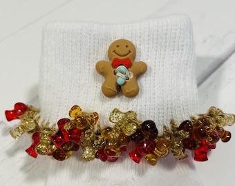 May include: White knitted baby socks with a gingerbread man button and a brown, red, and gold beaded trim.