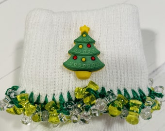 May include: White knitted socks with a green and yellow trim. The socks have a green Christmas tree button with a yellow star on top.