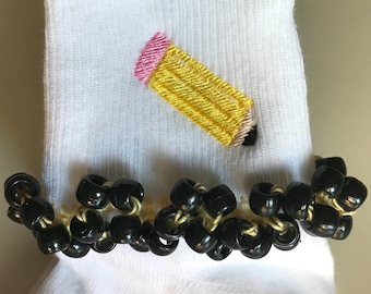 May include: White socks with a yellow pencil embroidered on the front. The socks have a black beaded trim around the top.