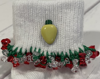 May include: White sock with a green and red trim and a yellow light bulb charm. The trim is made of beads.