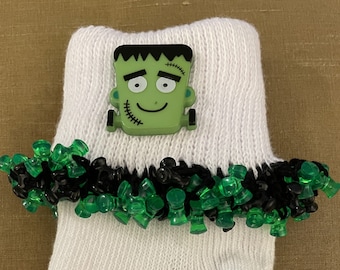 May include: White socks with a green and black trim. A green Frankenstein face is attached to the sock.