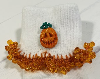 May include: White knitted baby socks with orange and white pumpkin button and orange beads around the cuff.